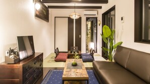 A traditional Japanese-style living room with tatami flooring, a low wooden table, a sofa, and a television on a cabinet. - Kyo Oyado Kurakura (Kyoto)