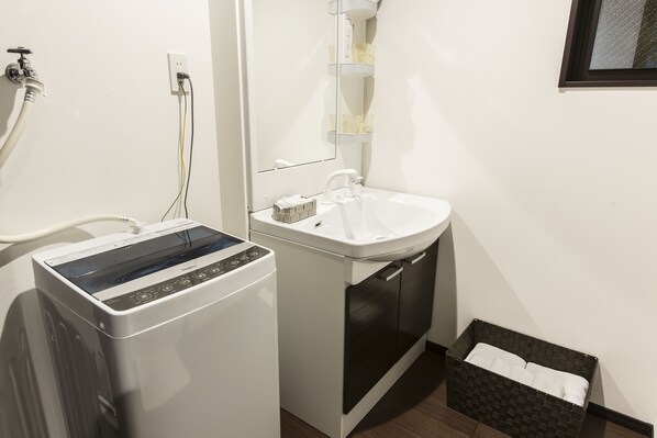 A compact bathroom with a washing machine, a sink, and a mirror.