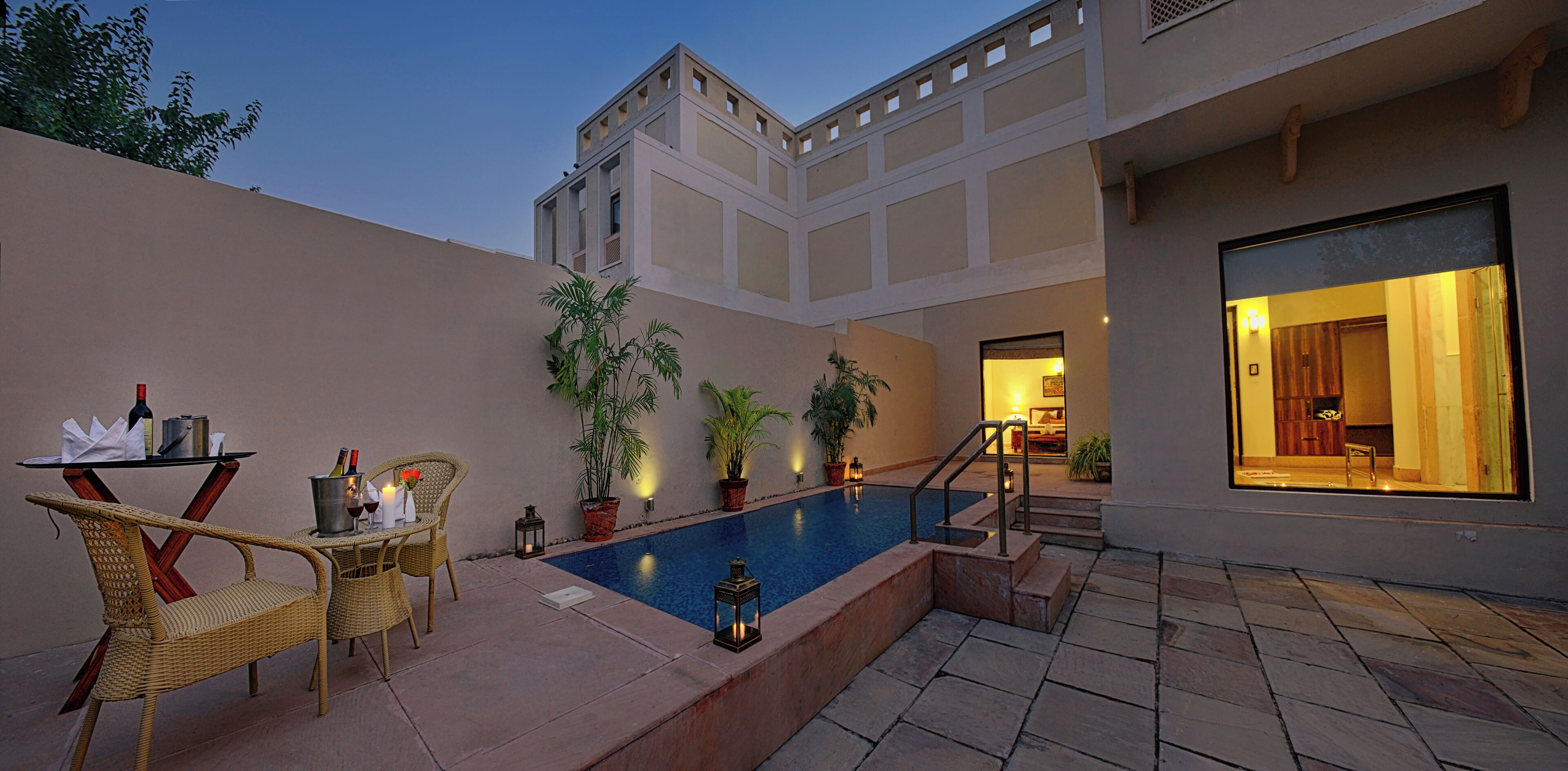 A pool area with lounge chairs, a table with bottles, and potted plants.