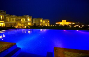 A nighttime view of a hotel with a swimming pool, illuminated buildings, and a clear sky. - Achrol Niwas A TreeHouse Hotel (Amer)