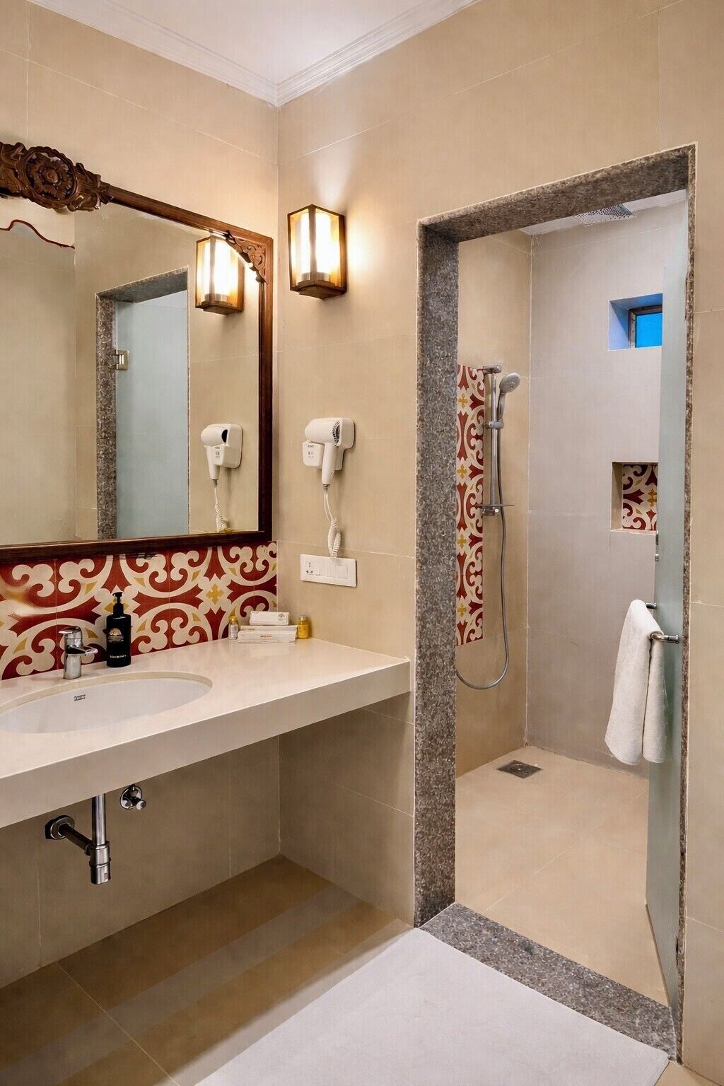 A bathroom with a double sink, a large mirror, a hairdryer, a shower with a handheld showerhead, and a towel rack.