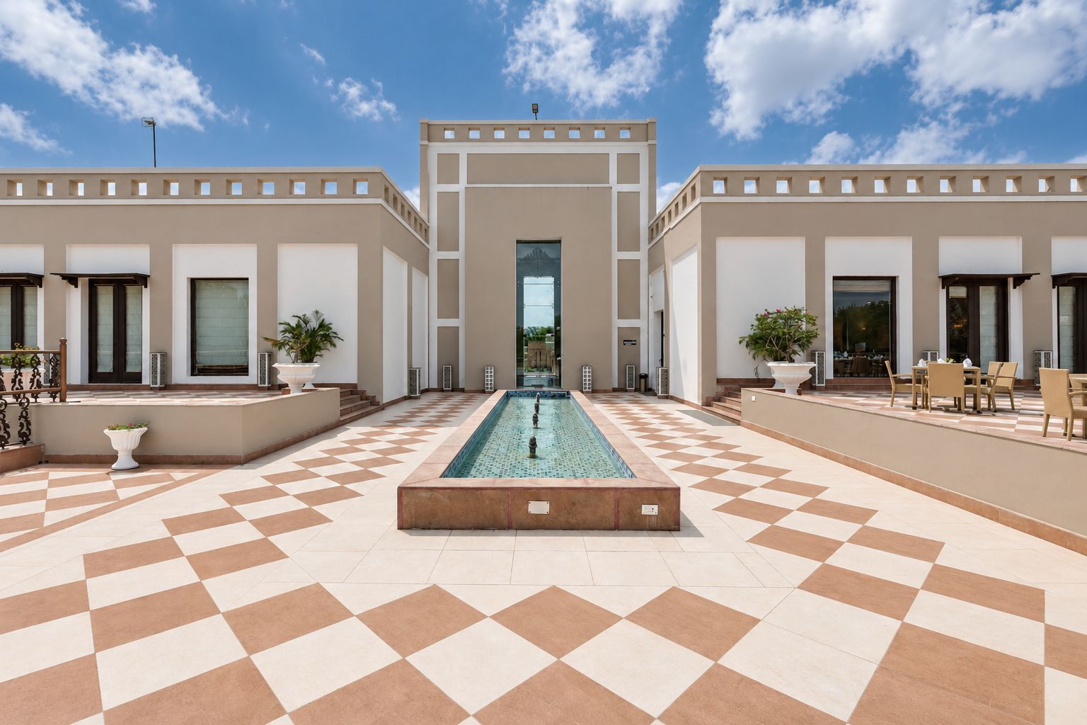 A hotel courtyard with a central pool, checkered flooring, and outdoor seating.