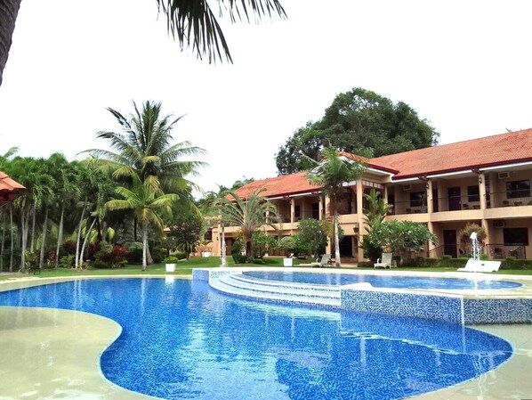 A hotel with a large pool, palm trees, and a red-roofed building.