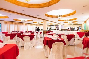 A banquet hall with tables covered in red tablecloths and white chairs, arranged in rows.