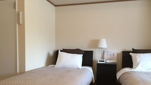 A hotel room with two single beds, a nightstand with a lamp, and a digital clock.