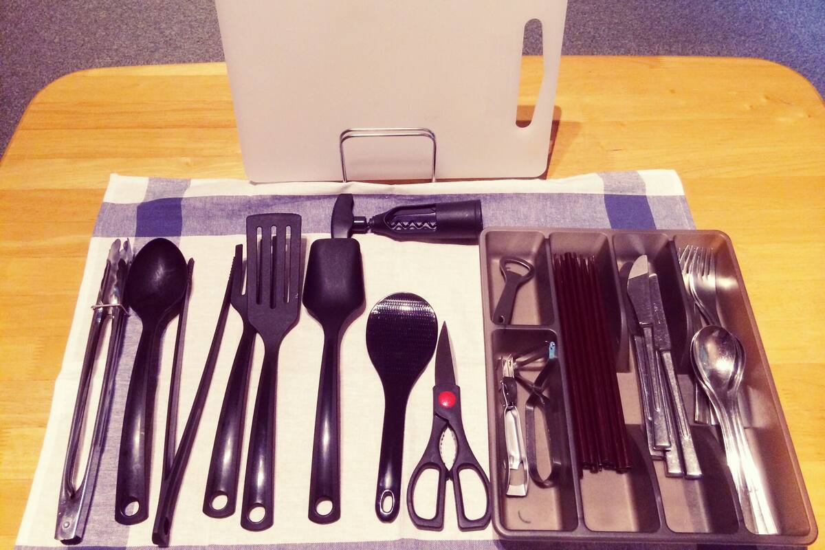 A table with a laptop, a set of black utensils, and a pair of scissors on a checkered cloth.