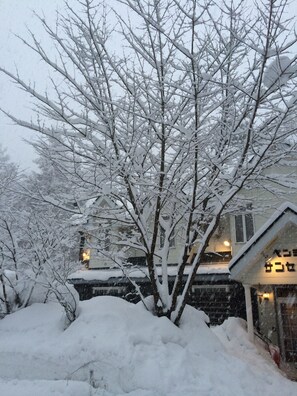 A snow-covered landscape with a house and a tree in the foreground. - Condominium Sunset Inn (Hakuba)