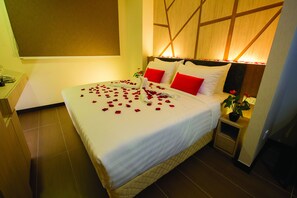 A neatly made bed with white linens and red pillows, a bedside plant, and rose petals on the bed. - Grand Orient Hotel Perai (Perai)