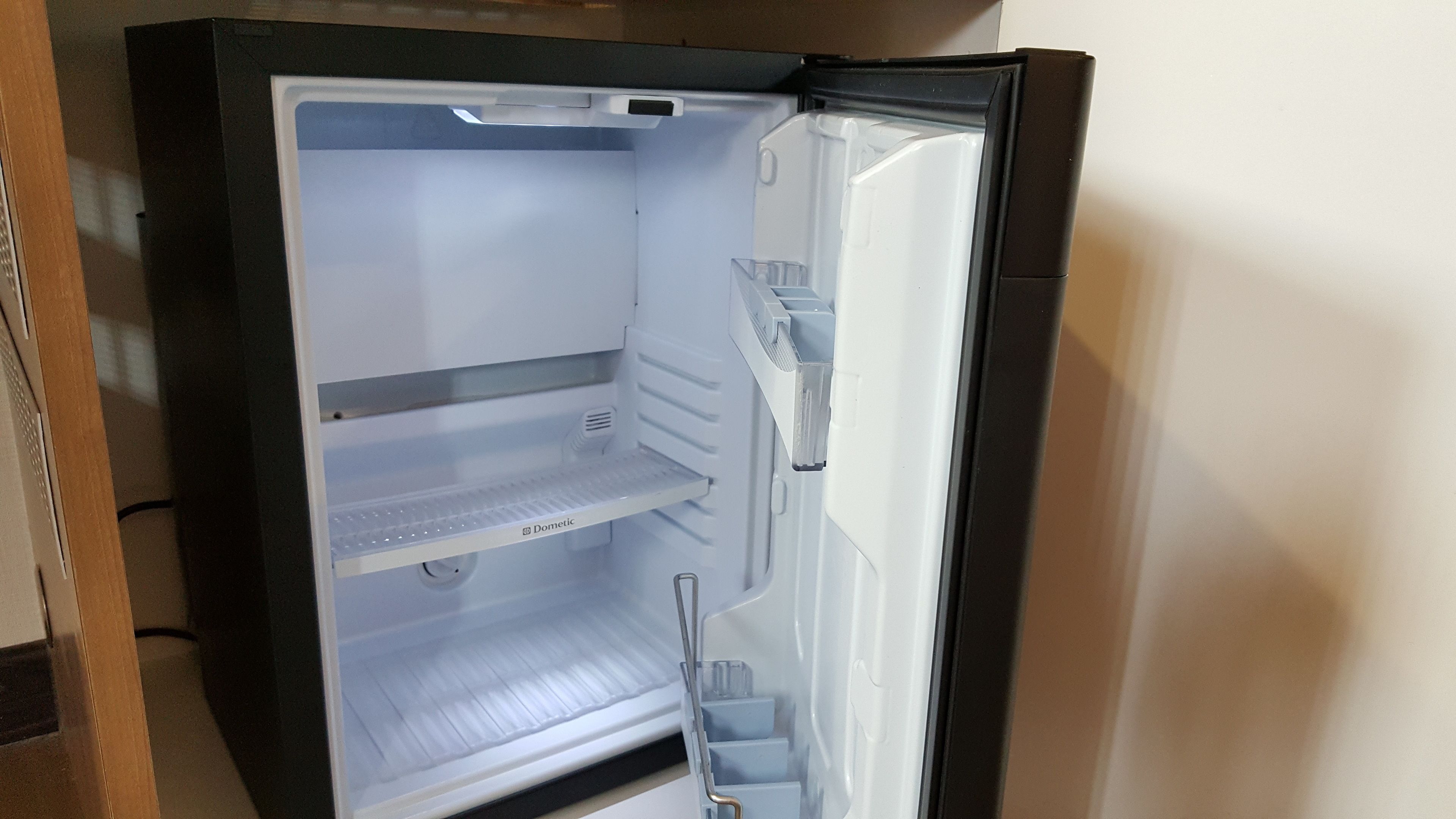 An open refrigerator with three shelves, a freezer compartment, and a water dispenser.