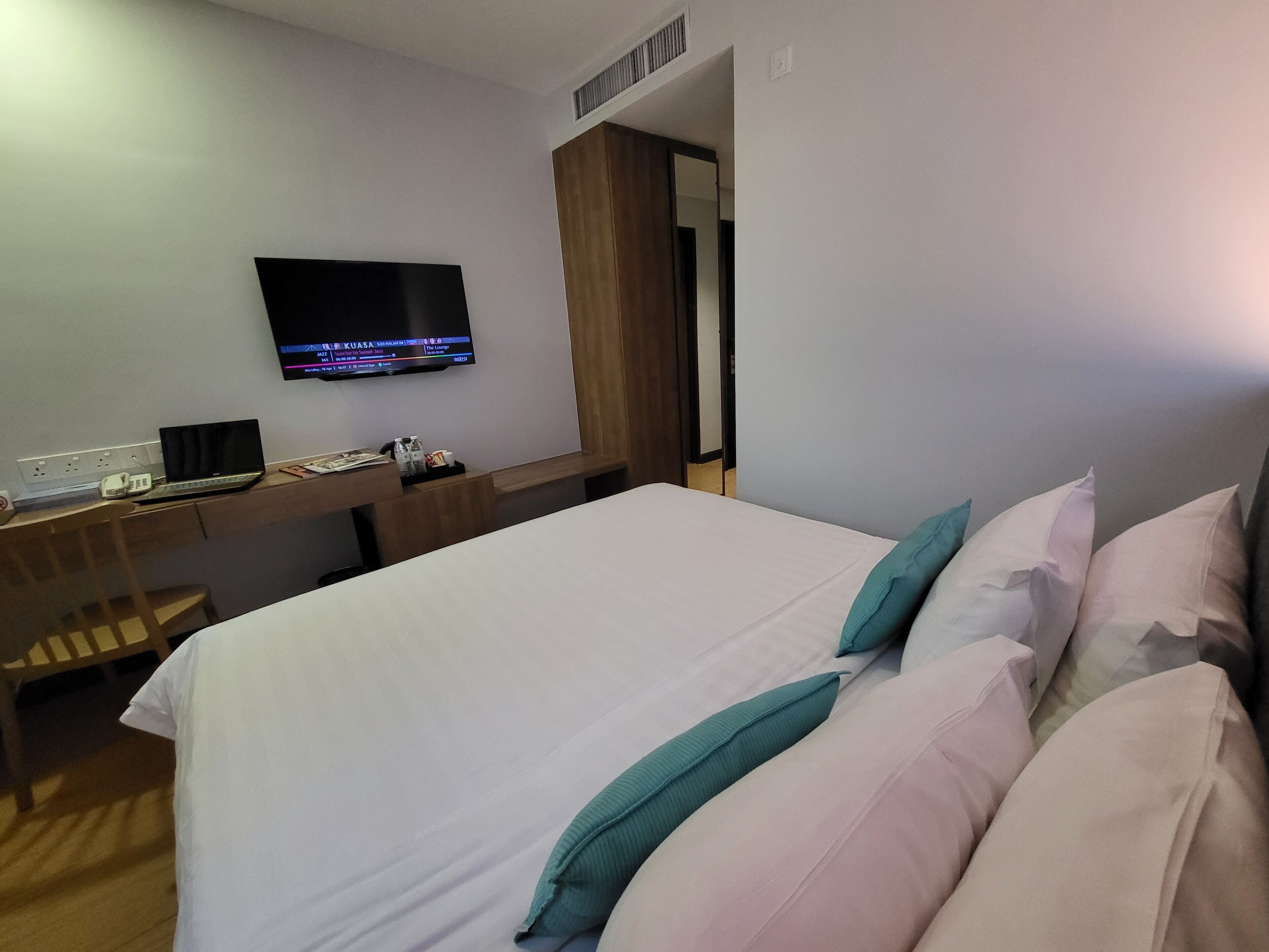 Habitación de hotel con cama, escritorio con computadora portátil, televisor y armario de madera.