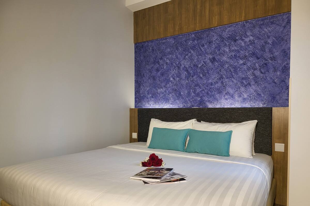A neatly made bed with white linens, a teal pillow, and a magazine on the bed.