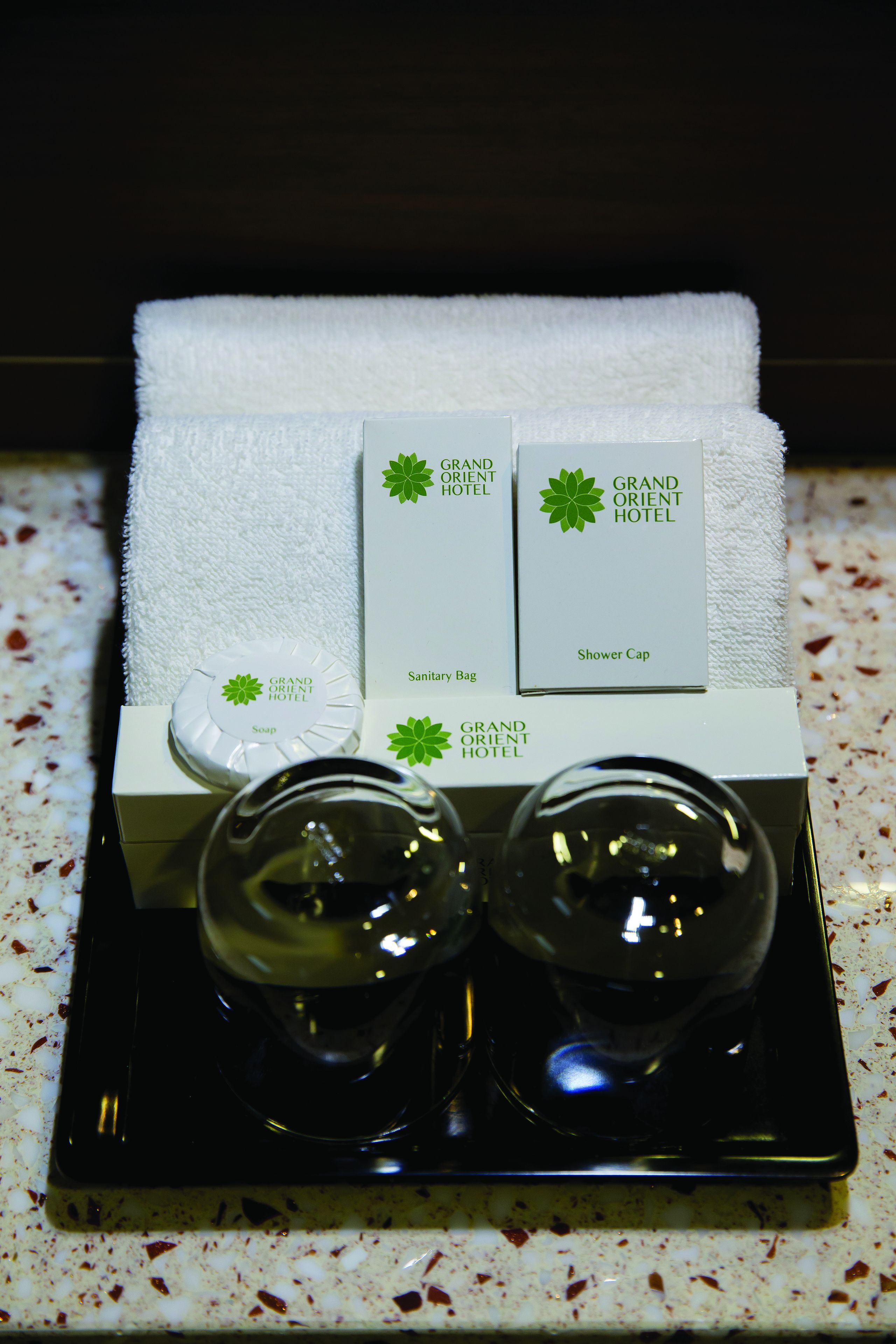 A tray with toiletries including a shower cap, sanitary bag, and soap, set on a speckled countertop.
