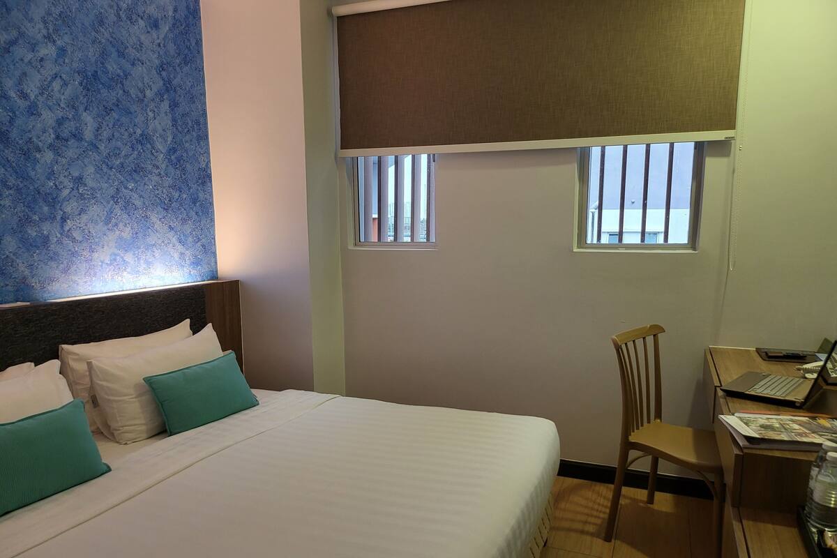 A hotel room with a bed, a desk, and two windows.