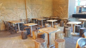 A restaurant interior with wooden tables and chairs, a stone wall with carved foliage, and a large mirror. - Grand Orient Hotel Perai (Perai)