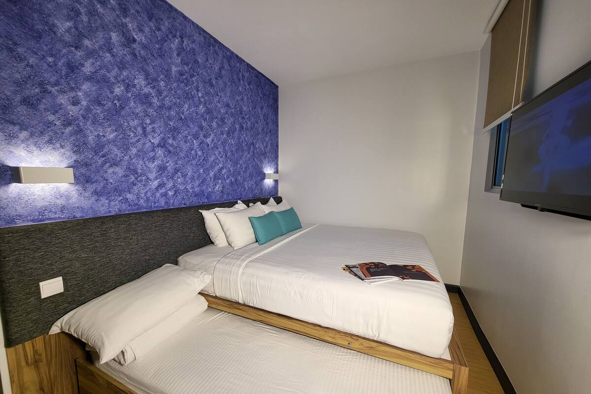 A hotel room with a bed, a wall-mounted TV, and a textured blue wall.