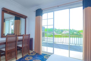 A hotel room with a large sliding glass door to a balcony, wooden chairs, a bed, and a patterned rug. - Galaxy Grand Hotel (Nuwara Eliya)