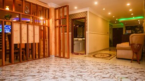 Un vestíbulo de hotel con un separador de madera, un televisor, un sofá y un piso estampado.