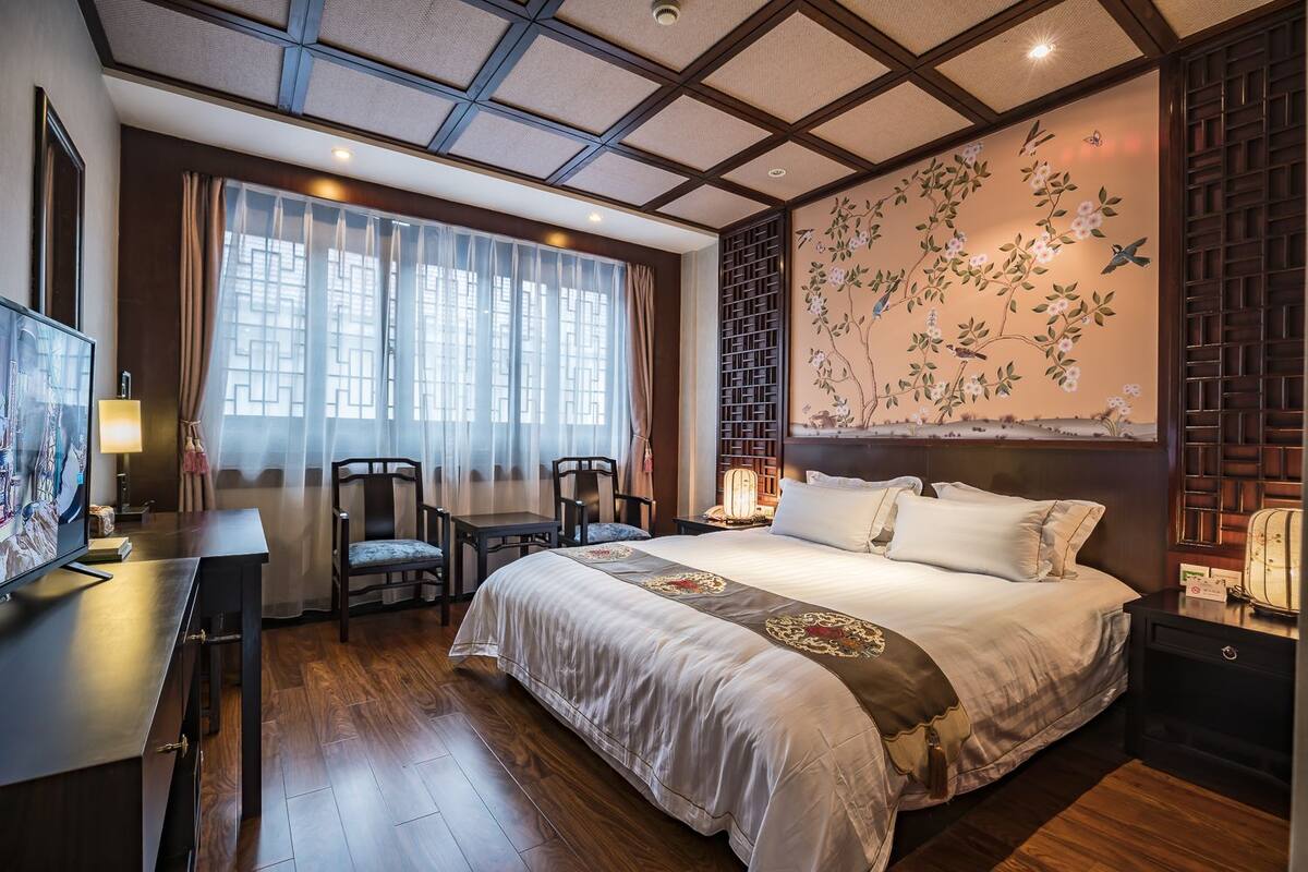 Habitación de hotel con una cama grande, un escritorio con silla, televisión y ventana con cortinas.