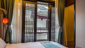 Ein Hotelzimmer mit Bett, Vorhängen, einer traditionellen Tür und Blick auf ein Gebäude.
