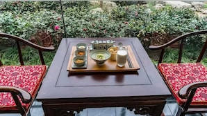 Ein Tisch ist mit einer Mahlzeit gedeckt, darunter Suppe, Reis und ein Getränk, in einem Raum mit Blick auf einen Garten.
