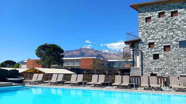 A swimming pool with lounge chairs, a stone building with balconies, and a mountain backdrop. - Hotel Camping Europa (Domaso)