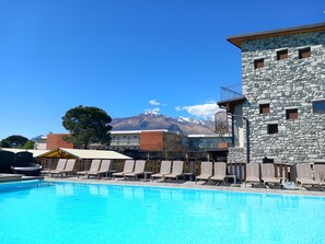 A swimming pool with lounge chairs, a stone building with balconies, and a mountain backdrop. - Hotel Camping Europa (Domaso)