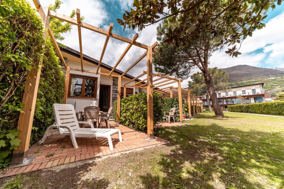 A covered patio with a wooden pergola, outdoor seating, and a view of a hillside.
