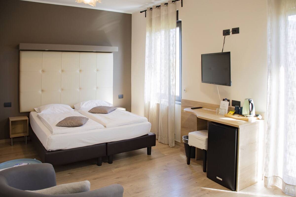 A hotel room with a bed, a desk, a chair, a TV, and a small refrigerator.