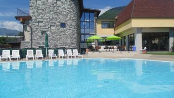 Una piscina con sillas de descanso, un edificio de piedra y un edificio amarillo con grandes ventanales.