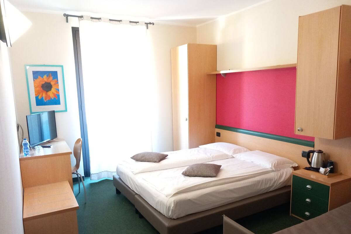 A hotel room with a bed, a desk, a chair, a coffee maker, and a picture of a sunflower on the wall.