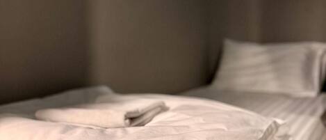 Una cama bien hecha con sábanas blancas en una habitación con pared gris y un cuadro colgado encima.