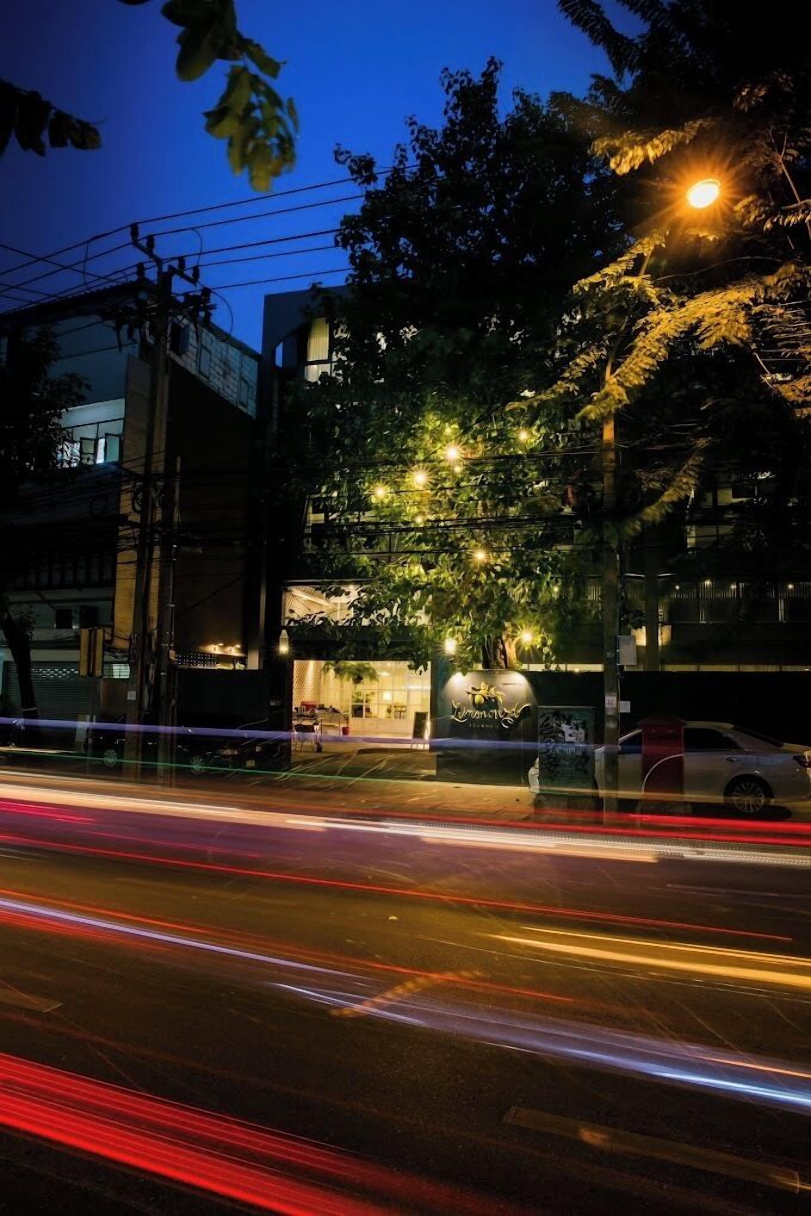 A nighttime urban street scene with a building featuring a large illuminated sign and a tree in front.