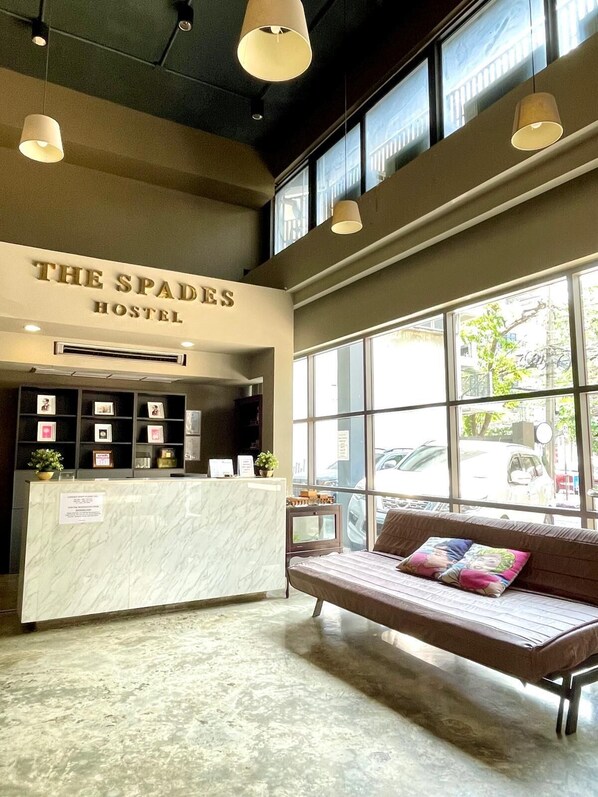 A reception area with a reception desk, a sofa with colorful cushions, and large windows offering a view of the street.