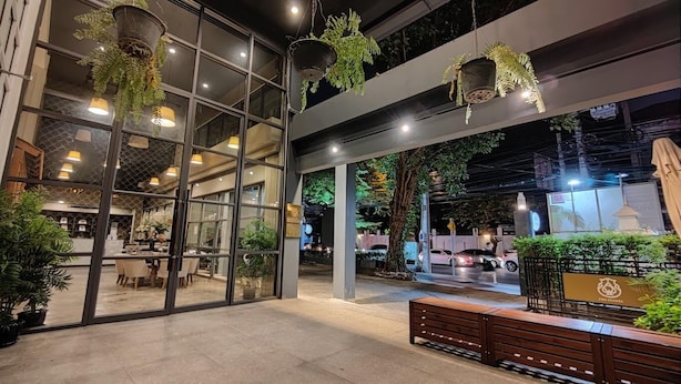 An indoor area with hanging plants, a bench, and a view of the street outside. - Collection O The Spades Hostel (Bangkok)