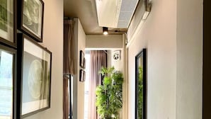 A hallway with framed pictures on the walls, a potted plant, and an air conditioning unit. - Collection O The Spades Hostel (Bangkok)