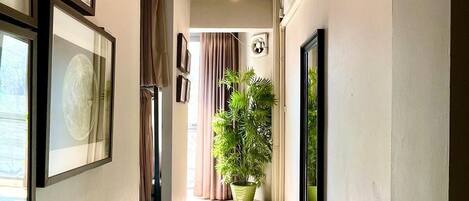 A hallway with framed pictures on the walls, a potted plant, and an air conditioning unit.