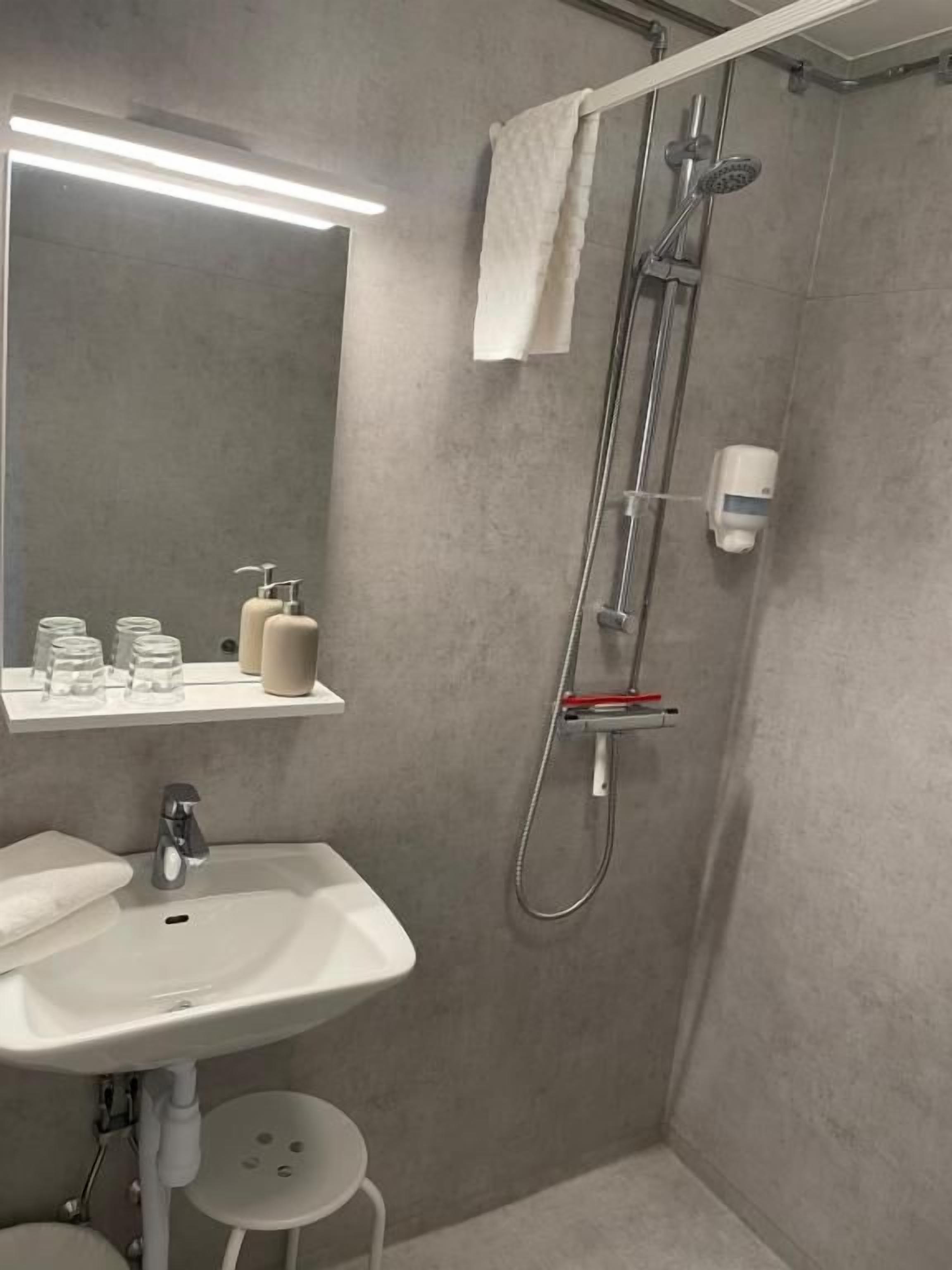 A bathroom with a sink, mirror, shower, and towel rack.