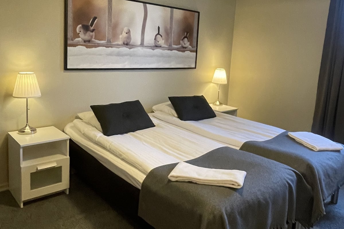 A hotel room with two beds, a painting of birds on the wall, and two bedside lamps.