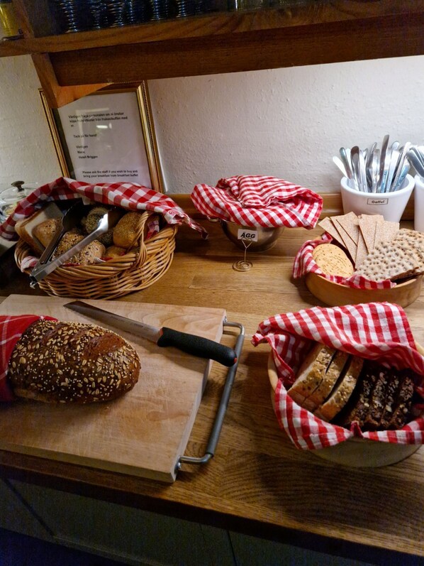 A variety of breads and pastries displayed on a wooden counter, with baskets and a knife.