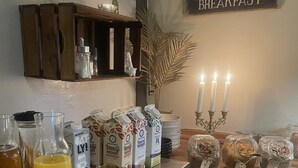 Una barra de desayuno con diversas opciones de comida y bebidas, como cartones de leche, una cafetera y frascos con conservas.
