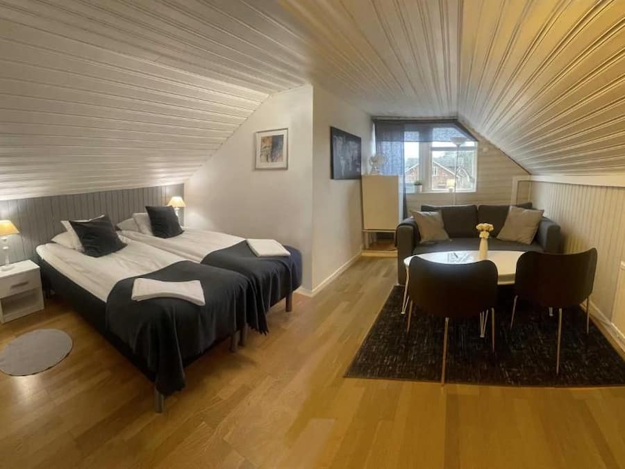 A bedroom with two beds, a sitting area with a table and chairs, and a window providing natural light.