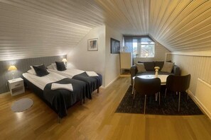 A bedroom with two beds, a sitting area with a table and chairs, and a window providing natural light. - Hotell Briggen i Åhus (Aahus)