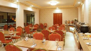 Zona pranzo con diversi tavoli e sedie, un'area buffet con vari piatti e una pentola grande sul lato destro.