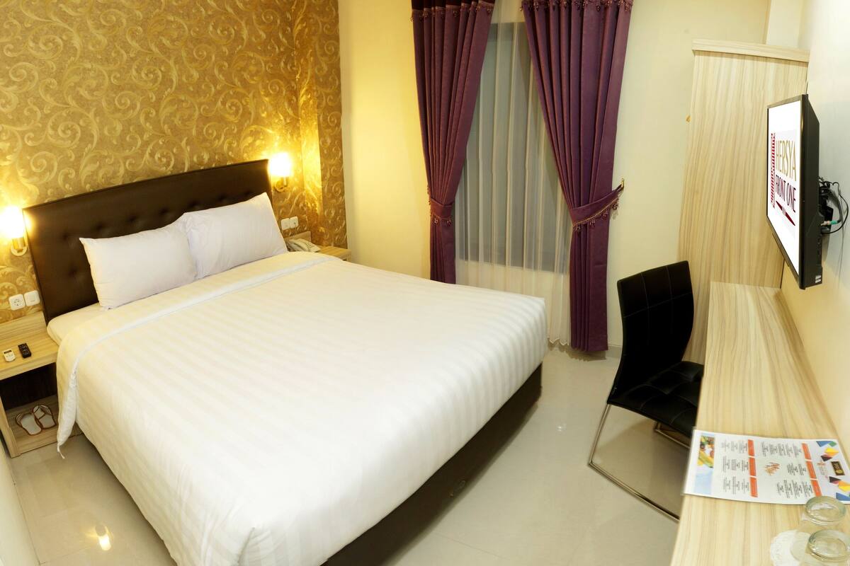 A hotel room with a large bed, a desk with a chair, a television, and a window with curtains.