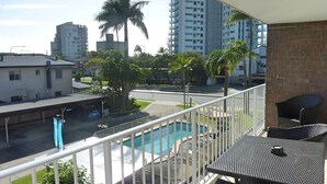 Un balcón con vista a una piscina, palmeras y edificios altos al fondo.