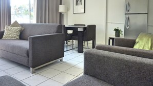 Una sala de estar moderna con sofás grises, una mesa de comedor y un refrigerador.