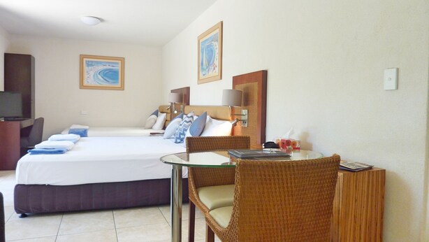 Habitación de hotel con cama, escritorio, silla, televisor y dos cuadros en la pared.