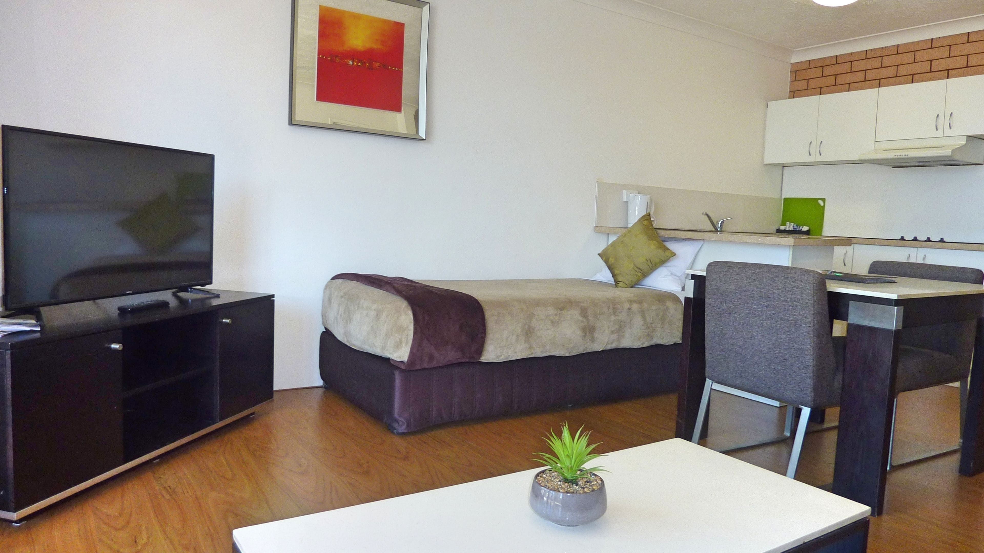 Una habitación pequeña y moderna con cama, televisor, escritorio y kitchenette.