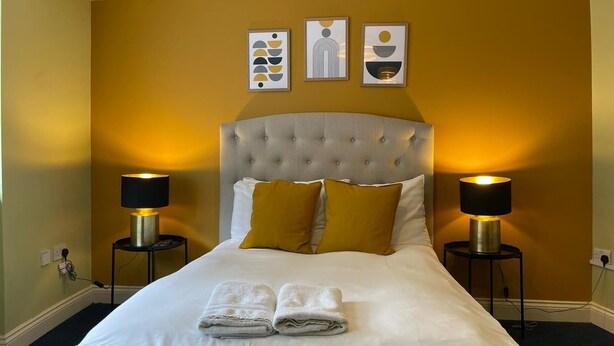 A hotel room with a large bed, two bedside lamps, and three wall art pieces. - Brighter Properties (London)