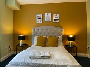 A hotel room with a large bed, two bedside lamps, and three wall art pieces. - Brighter Properties (London)
